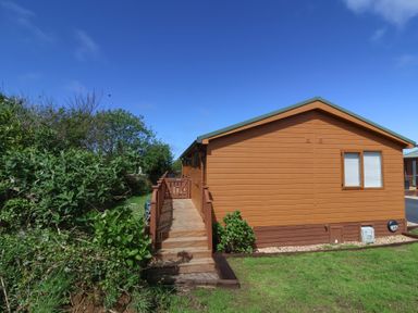 A wooden cabin with a ramp and green bushes at Poppy Lodge in Mullacott Ilfracombe
