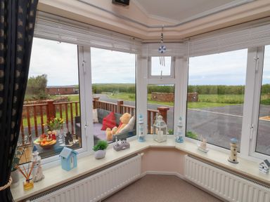 A bay window with small decorative items and a view of a patio with a sofa and teddy bear at Poppy Lodge in Mullacott Ilfracombe