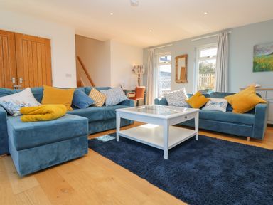 A living room with blue sofas yellow cushions white coffee table and wooden doors at Chilowan in Trewarmett near Tintagel