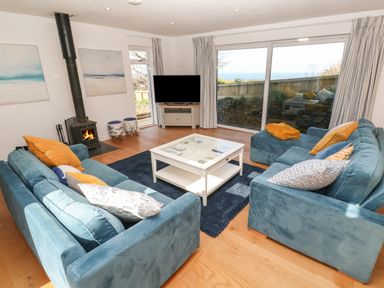 A living room with blue sofas a white coffee table and a wood burning stove at Chilowan in Trewarmett near Tintagel