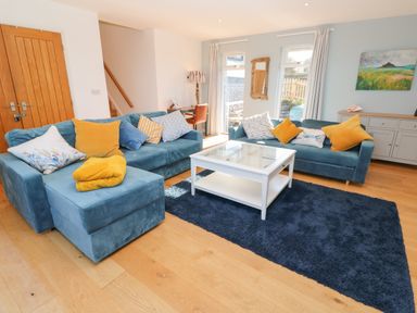 A living room with blue sofas and yellow cushions a white coffee table and wooden floor at Chilowan in Trewarmett near Tintagel