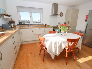 A kitchen with a round table and four wooden chairs a vase with flowers on the table and cabinets along the walls at Chilowan in Trewarmett near Tintagel