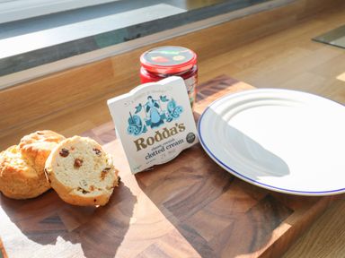 Scones with clotted cream and jam on a wooden cutting board next to a white plate on a wooden surface at Chilowan in Trewarmett near Tintagel