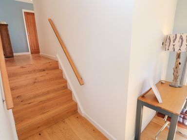 Wooden stairs with a handrail leading up to a hallway with a closed wooden door and a small table with a lamp to the side at Chilowan in Trewarmett near Tintagel