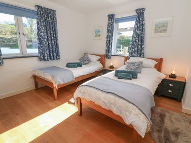 A bedroom with two single beds wooden furniture and blue curtains at Chilowan in Trewarmett near Tintagel