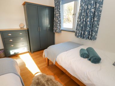 A bedroom with two single beds a chest of drawers wardrobe window with patterned curtains and wooden floor at Chilowan in Trewarmett near Tintagel