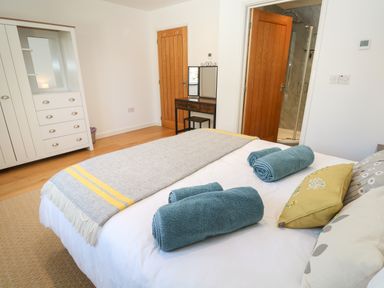 A bedroom with a bed with rolled towels and pillows a dresser with a mirror and two wooden doors at Chilowan in Trewarmett near Tintagel