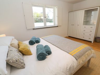 A bedroom with a bed with rolled towels and cushions near a window and a white wardrobe at Chilowan in Trewarmett near Tintagel