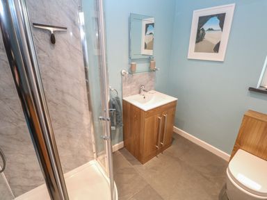 A bathroom with a shower cubicle a wooden vanity unit with a sink a toilet and wall art at Chilowan in Trewarmett near Tintagel