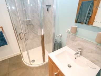 A bathroom with a corner glass shower enclosure a sink with a faucet and a mirror at Chilowan in Trewarmett near Tintagel