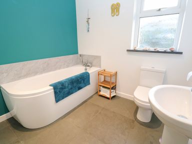 A bathroom with a bathtub a toilet a sink and a small wooden shelf at Chilowan in Trewarmett near Tintagel