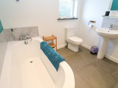 A bathroom with a bathtub a toilet a pedestal sink and a small wooden shelf at Chilowan Trewarmett near Tintagel