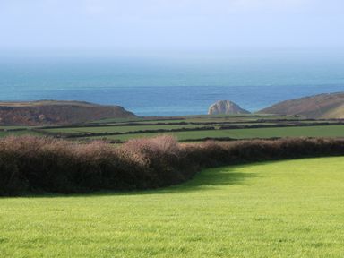 A grassy field with hedges and a view of the ocean with hills in the distance at Chilowan in Trewarmett near Tintagel