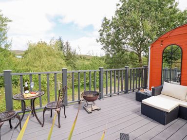 An outdoor deck with a table, chairs, and a grill at Red Kite at Wild Valley Huts in Llanrhaeadr-Ym-Mochnant