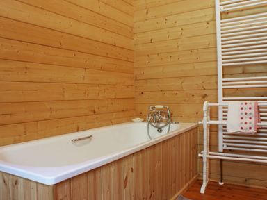 A bathroom with a bathtub and wooden panel walls and a white towel rail with a towel at Valley Lodge Oakfordbridge near Bampton