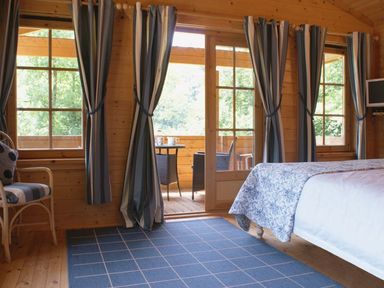 A bedroom with striped curtains blue rug and a chair near windows at Valley Lodge Oakfordbridge near Bampton