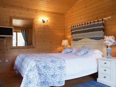 A bedroom with a double bed bedside tables lamps and a wall mounted television at Valley Lodge in Oakfordbridge near Bampton