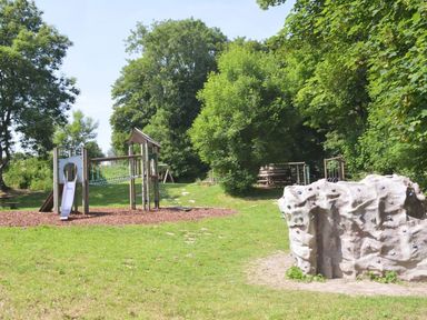 A playground with a slide climbing frame and a rock climbing wall surrounded by grass and trees at Valley Lodge in Oakfordbridge near Bampton