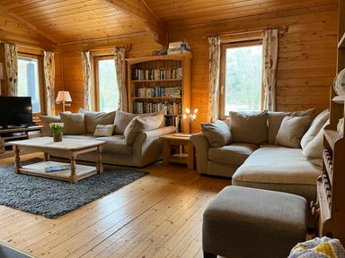 A living room with two sofas a wooden coffee table a bookshelf and windows at Valley Lodge Oakfordbridge near Bampton