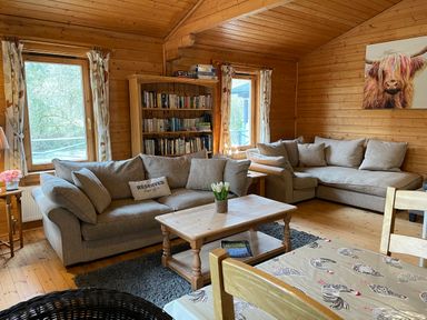 A living room with two gray sofas a wooden coffee table a bookshelf and a dining table at Valley Lodge Oakfordbridge near Bampton