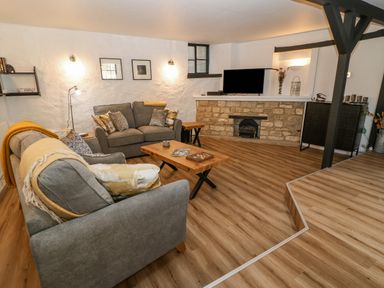 A living room with two grey sofas wooden coffee tables a small fireplace and a television at Ellie's Cottage in Burford