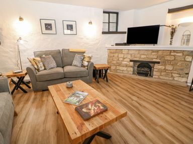 A living room with grey sofas wooden tables a television on a stone fireplace at Ellie's Cottage in Burford