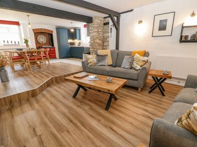 A living room with two grey sofas a wooden coffee table and side table dining table with chairs and blue kitchen cabinets at Ellie's Cottage in Burford