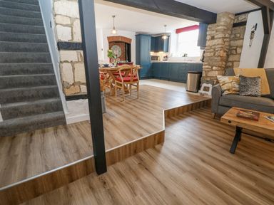 An open plan living area with wooden flooring a grey sofa and blue kitchen cabinets at Ellie's Cottage in Burford