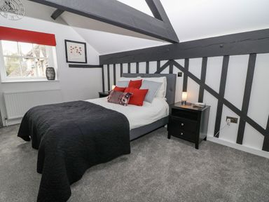 A bedroom with a bed with black quilt and red pillows and black beams on walls at Ellie's Cottage in Burford