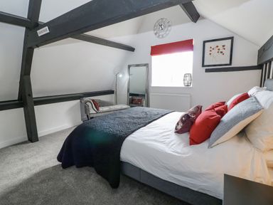 A bedroom with a bed with red and grey pillows a chaise lounge a standing mirror and a window with a red blind at Ellie's Cottage in Burford