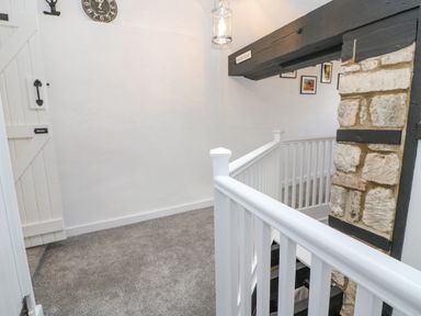 A staircase landing with white wooden railing stone pillar and a wall clock at Ellie's Cottage in Burford