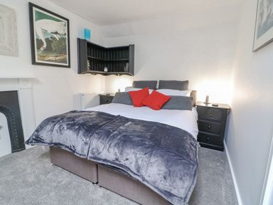 A bedroom with a bed with gray and red pillows and a gray blanket at Ellie's Cottage in Burford