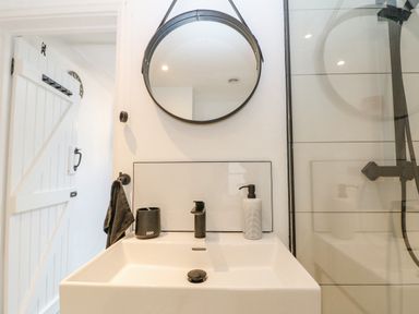 A bathroom sink with black soap dispenser and toothbrush holder under a round mirror at Ellie's Cottage in Burford