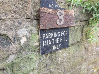 A stone wall with a sign for parking at 141a The Hill and the number 3 mounted on wood at Ellie's Cottage in Burford
