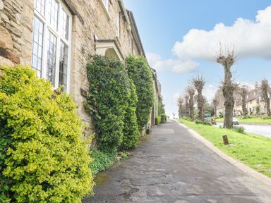 A pavement beside stone houses with trimmed bushes and leafless trees along a road at Ellie's Cottage in Burford