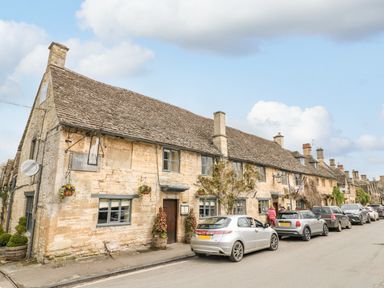 A stone building with a thatched roof and cars parked outside on the street at Ellie's Cottage in Burford