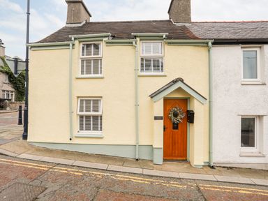 Exterior view of a yellow cottage with a wooden door and two windows at Bwthyn Lili (Lily Cottage) in Cemaes Bay