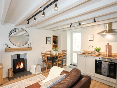 A kitchen and dining area with a wood burner fireplace and wooden table with chairs at Bwthyn Lili (Lily Cottage) in Cemaes Bay