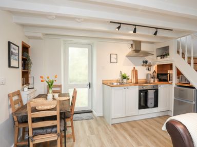 A kitchen with a dining table chairs stove and refrigerator at Bwthyn Lili (Lily Cottage) in Cemaes Bay