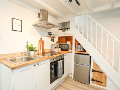 A kitchen with a sink stove oven refrigerator microwave toaster and wooden cabinets under a staircase at Bwthyn Lili (Lily Cottage) in Cemaes Bay