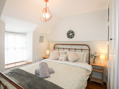 A bedroom with a bed with pillows and folded towels and bedside tables with lamps and flowers at Bwthyn Lili in Cemaes Bay