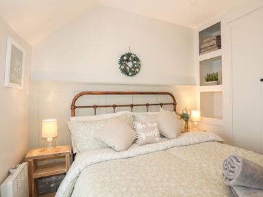 A bedroom with a bed with pillows and blankets two bedside tables with lamps and shelves with towels and plants at Bwthyn Lili (Lily Cottage) in Cemaes Bay