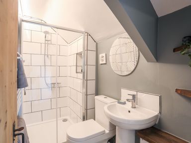A bathroom with a shower, toilet, sink, mirror, and wooden shelves at Bwthyn Lili (Lily Cottage) in Cemaes Bay