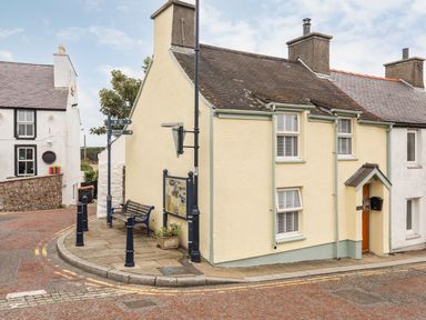 A street corner with a yellow two-story house a bench and signposts at Bwthyn Lili (Lily Cottage) in Cemaes Bay