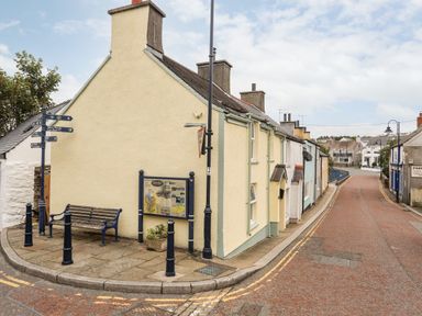A street corner with pastel colored houses a bench street signs and a lamppost at Bwthyn Lili (Lily Cottage) in Cemaes Bay