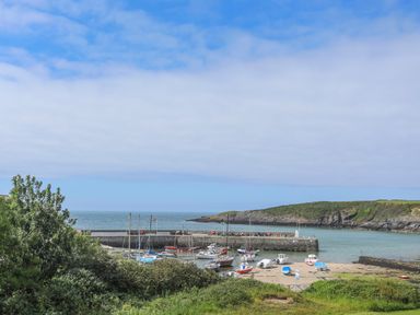 A small harbor with boats docked near a stone pier with green hills and ocean in the background at Bwthyn Lili (Lily Cottage) in Cemaes Bay