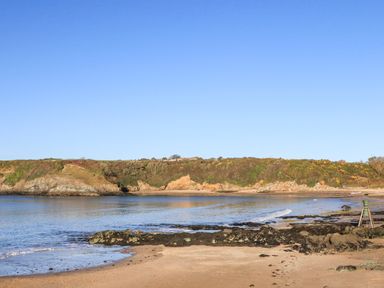 A beach with rocky shore and calm water under a clear sky at Bwthyn Lili (Lily Cottage) in Cemaes Bay