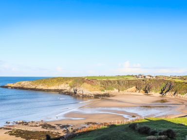 A coastal bay with sandy beach and rocky cliffs with buildings on grassy land at Bwthyn Lili (Lily Cottage) in Cemaes Bay