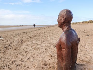 A rusty metal sculpture of a person on a sandy beach with a person walking in the distance at Ismay Dining Room Suite - Titanic Interest in Waterloo Merseyside