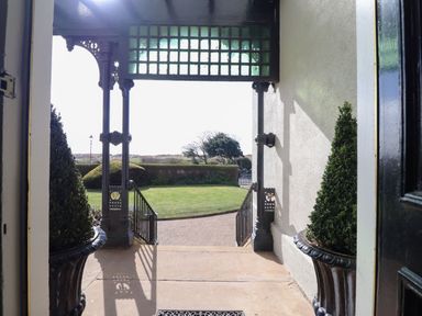 An outdoor porch area with ornate metal columns and railings overlooking a garden with trimmed bushes and a paved pathway at Ismay Dining Room Suite Titanic Interest Waterloo Merseyside
